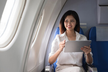 Asian woman using tablet on airplane. Concept of air travel, digital technology, and in-flight entertainment