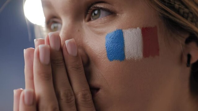 French sports fan is worried. Close-up of face of young fan with flag of France on her face, woman watches match, competition, game and is worried, cheers for France
