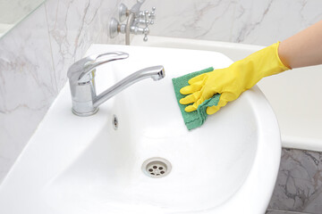 female cleaner in yellow rubber gloves washes the sink in the bathroom with a rag. general cleaning...