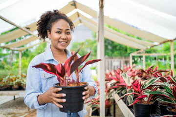 A woman is holding a plant in a black pot. She is smiling and she is happy