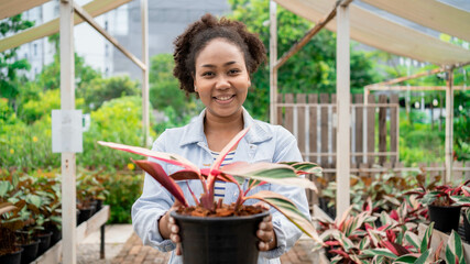 A woman is holding a plant in a black pot. She is smiling and she is happy