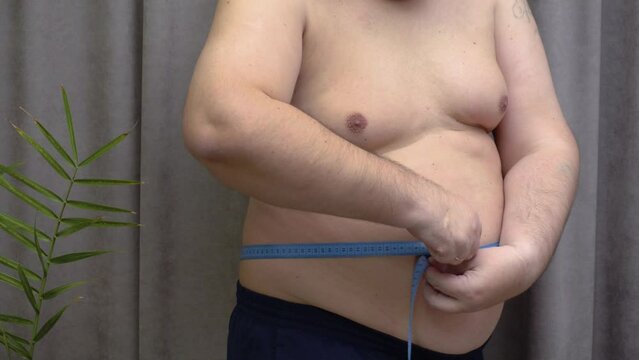 A fat man measures his waist with a measuring tape. Suitable for content about weight loss, weight loss, healthy eating.