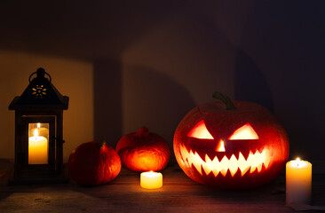 Halloween pumpkin head jack lantern with burning candles on old wooden table.