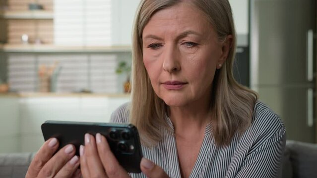 Shocked anxious 70s retired senior Caucasian woman elderly female grandmother looking mobile phone cellphone pensioner read message getting bad scam notification bank debt health medical problems home