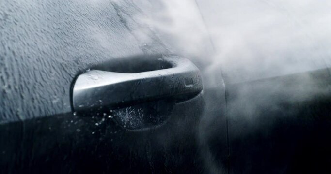Super slow motion macro of modern auto vehicle detail under high pressure water jet during washing process on self service car wash. Manual car wash with pressurized water spray.