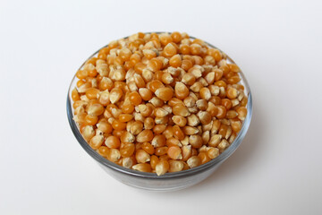 Dried corn kernels full in glass transparent bowl, isolated on white background