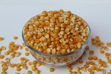 Dried corn kernels full in glass transparent bowl, isolated on white background