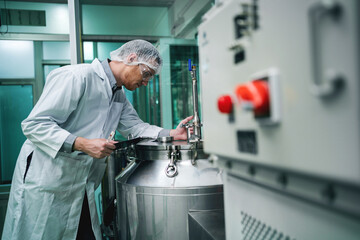 A man in a white lab coat is working on a machine. The machine is large and has a red button on it