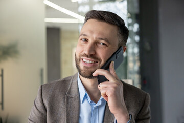 Smiling business professional in a modern office environment having a phone conversation on a smartphone.