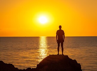 Silhouette of man standing on rock in front of sunset over calm sea