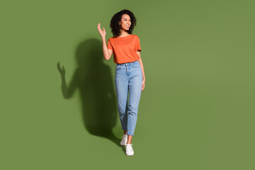 Full length photo of lovely young lady look wave hand empty space walk dressed stylish orange garment isolated on khaki color background