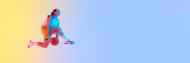 Banner. Focused on game young woman, basketball player dribbling in mid-air in neon light against...