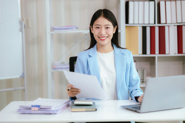 Portrait of a young Asian business woman working on Stacks of paper files to find and check unfinished documents in a folder document in a busy job.