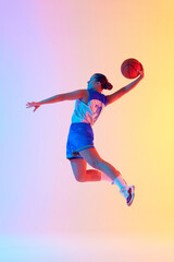 Young athletic woman, basketball player doing perfect slam dunk in motion in neon light against...