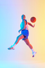 Athletic woman in blue basketball outfit, ready to make play in neon light against gradient studio background. Concept of professional sport, championship, tournament, hobby and recreation. Ad