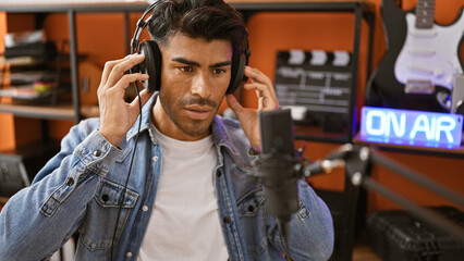 Handsome hispanic man with beard in studio wearing headphones preparing to record music