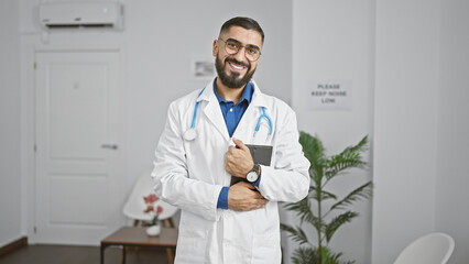 Smiling young arab man doctor standing confidently in a modern clinic waiting room.