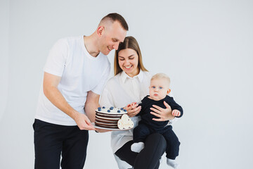 Happy family couple with baby son in arms and sweet cake on white background. Young parents with their son on a white background.