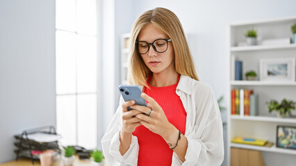 A focused young woman using her smartphone in a modern office setting.