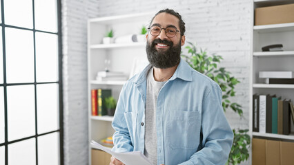 Handsome hispanic man with beard smiling in an office, exuding professionalism and approachability.