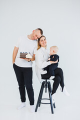 Happy family couple with baby son in arms and sweet cake on white background. Young parents with their son on a white background.