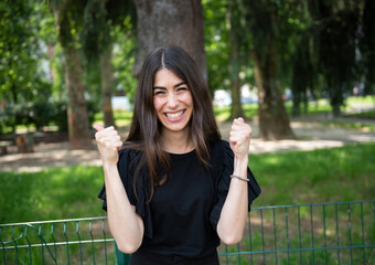 Euphoric young woman smiling with clenched fists in a gesture of victory, enjoying a sunny day in...