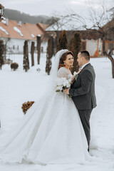 A bride and groom are standing in the snow, the bride holding a bouquet and the groom holding a bouquet