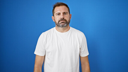 Fototapeta premium Hispanic mature man with grey hair wearing a white shirt against a blue wall outdoors