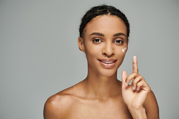 A beautiful young African American woman, topless, holds up a peace sign against a grey background.