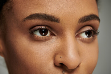 Close-up of a young African American woman with stunning brown eyes, skincare routine, on a grey...