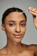 African American woman in strapless top holding serum pipette on a grey backdrop.