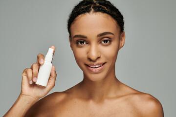 Young African American woman in strapless top holds lotion bottle, prioritizing skin care routine...