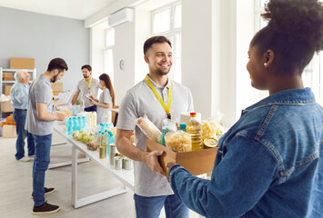 Afro american woman getting food box help from young volunteer working in charitable food...