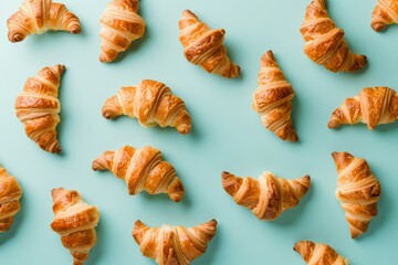 Croissants arranged on light blue background in a flat lay style