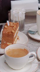 A cup of coffee with milk and a tasty cake on a table in a cozy cafe