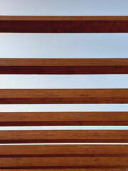 Wooden beams under blue sky. Solid dark wooden blocks in horizontal pattern background. Architecture and construction concept. Full frame.