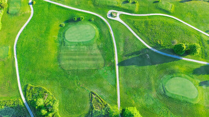 Straight aerial view cart path in 18 holes golf course, lavish greens sloping fairways, lots of...