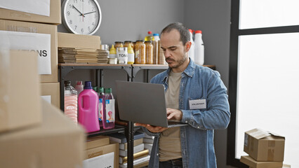 Bearded man using laptop in warehouse with donations and supplies
