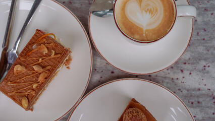 A cup of coffee with milk and a tasty cake on a table in a cozy cafe