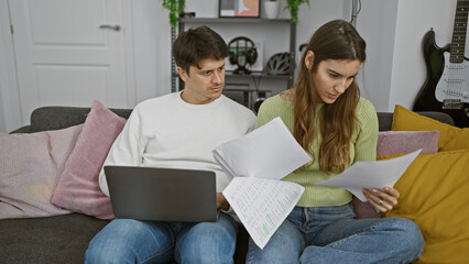 A concerned man and woman review documents together on a couch in a cozy living room, surrounded by modern decor.