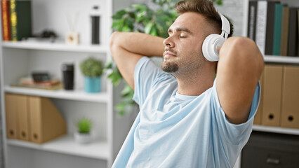 Relaxed young hispanic man wearing headphones enjoys music indoors.