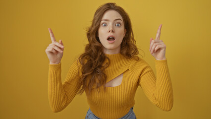 Attractive young blonde woman surprised over isolated yellow background, wearing a yellow sweater...
