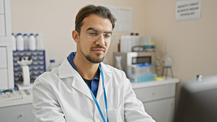 Handsome young hispanic man with beard wearing glasses and lab coat in a scientific laboratory setting