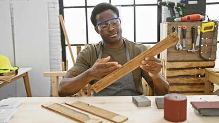 A focused young man inspects timber in a woodwork studio, surrounded by tools reflecting his craft.