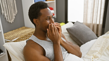 Young african american man yawning in a cozy bedroom setting, depicting a morning routine.