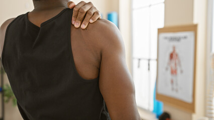 African american man receiving shoulder therapy in a modern rehabilitation clinic room.