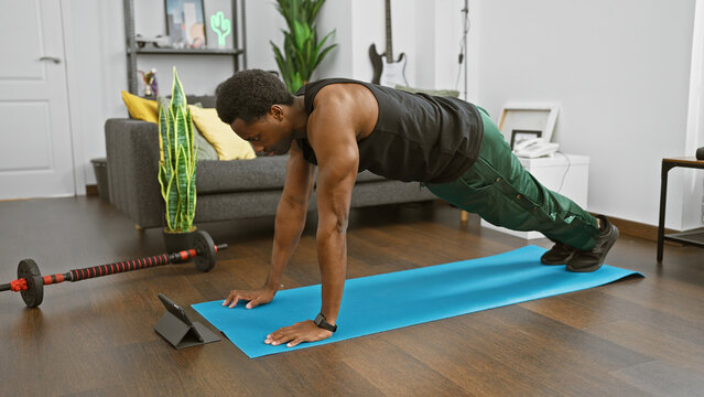 A fit african american man doing push-ups at home while following a workout video on his tablet. - Powered by Adobe