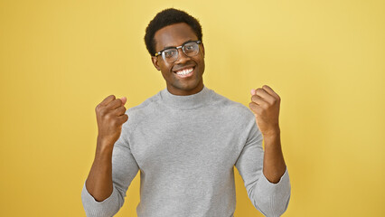 Cheerful young adult african american man with glasses over yellow background showing success...
