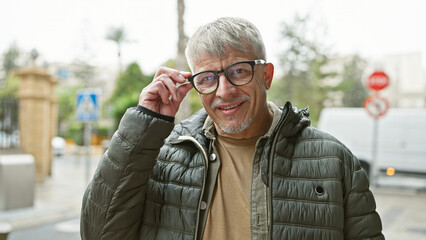 Mature man with glasses smiling in an urban outdoor setting, showcasing city living and active...