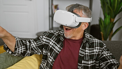 Excited middle-aged man with grey hair using virtual reality headset in a modern living room.